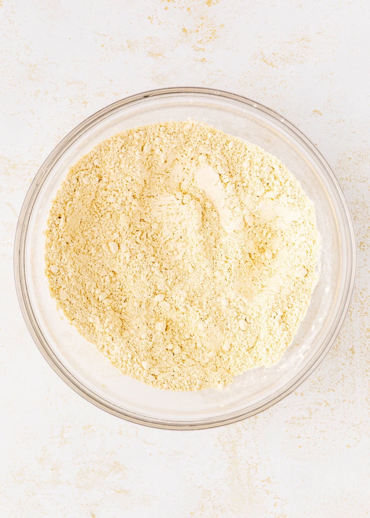 A glass bowl filled with yellow cornmeal on a white surface.