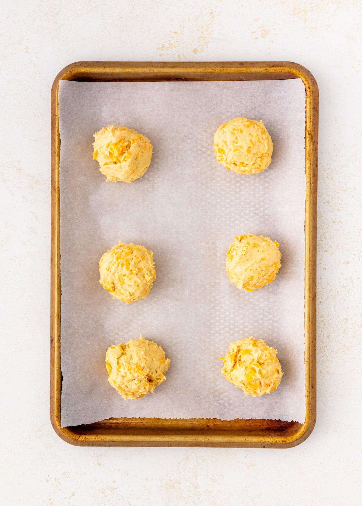 Six balls of dough on a parchment-lined baking sheet, ready to be baked.