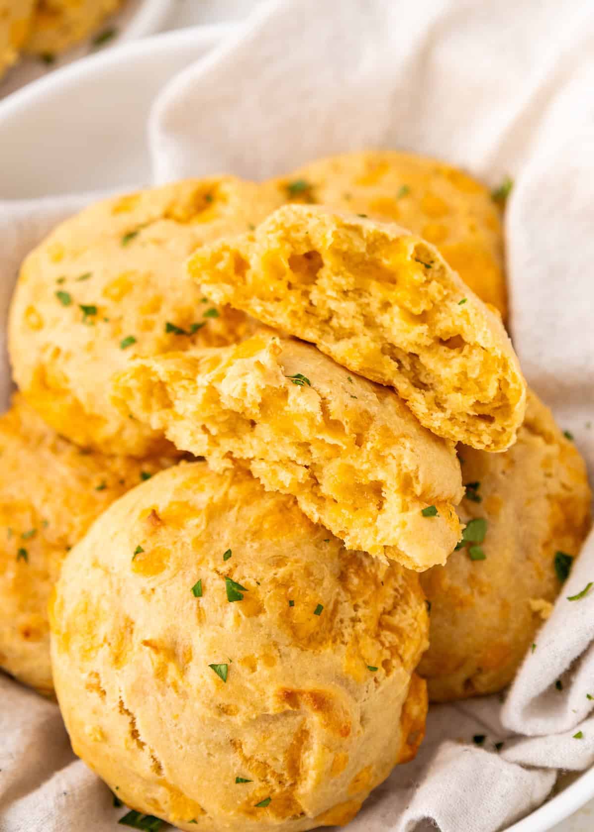 Golden cheddar biscuits with herbs, one broken open to show fluffy, cheesy inside.